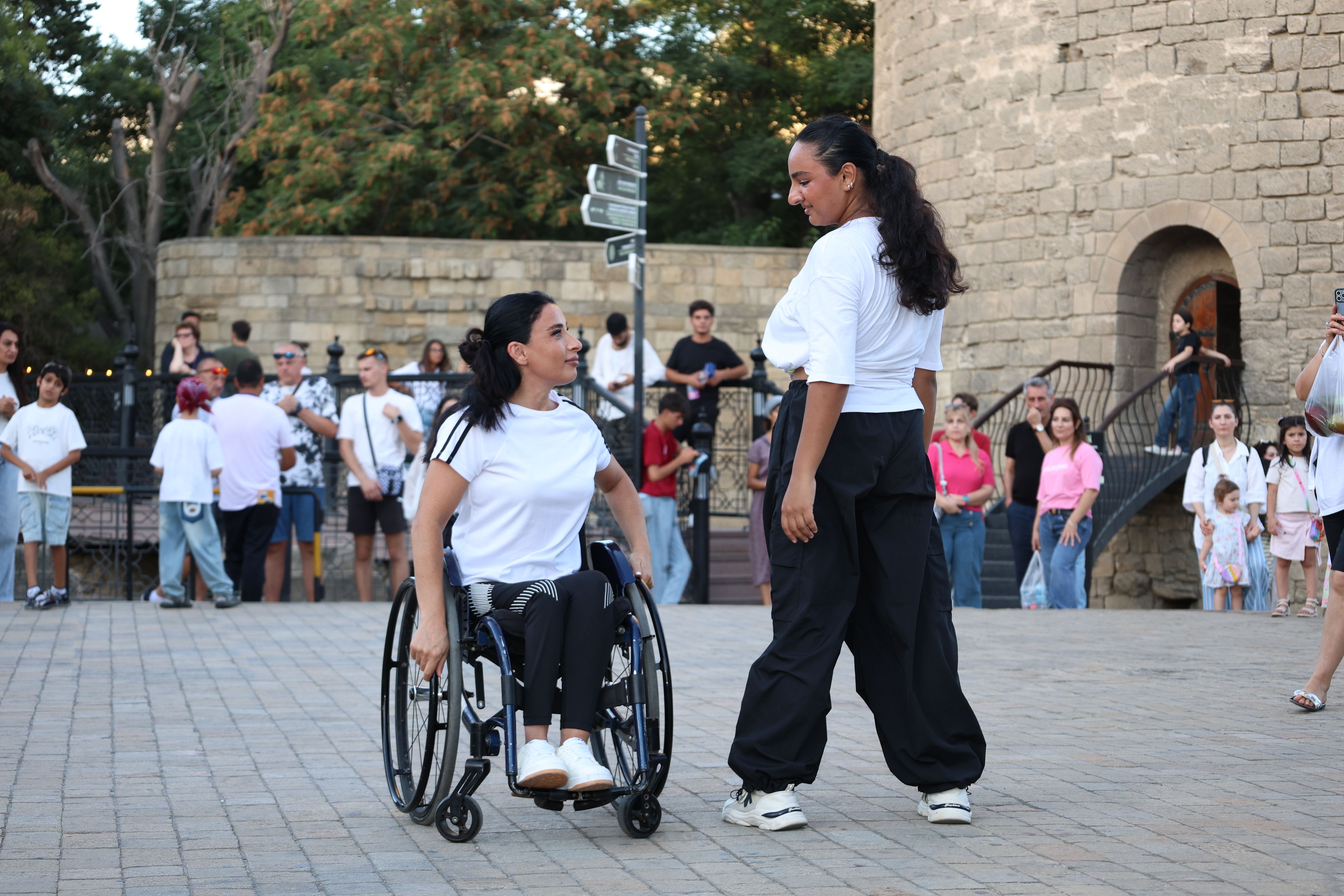 Two women, including one wheelchair user, performing outdoors in front of an audience, representing inclusive event design.