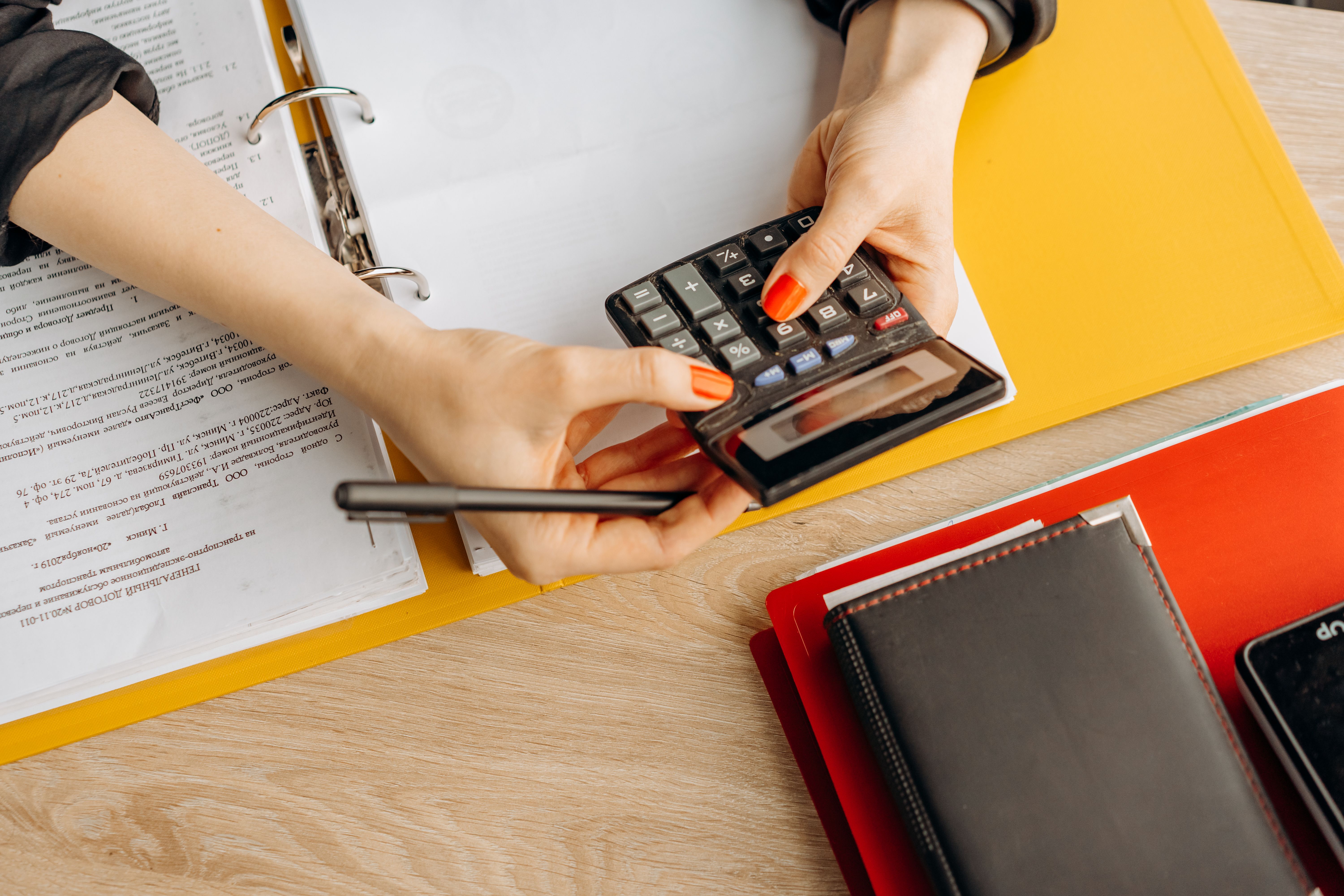 Hands using a calculator beside documents and folders at a desk