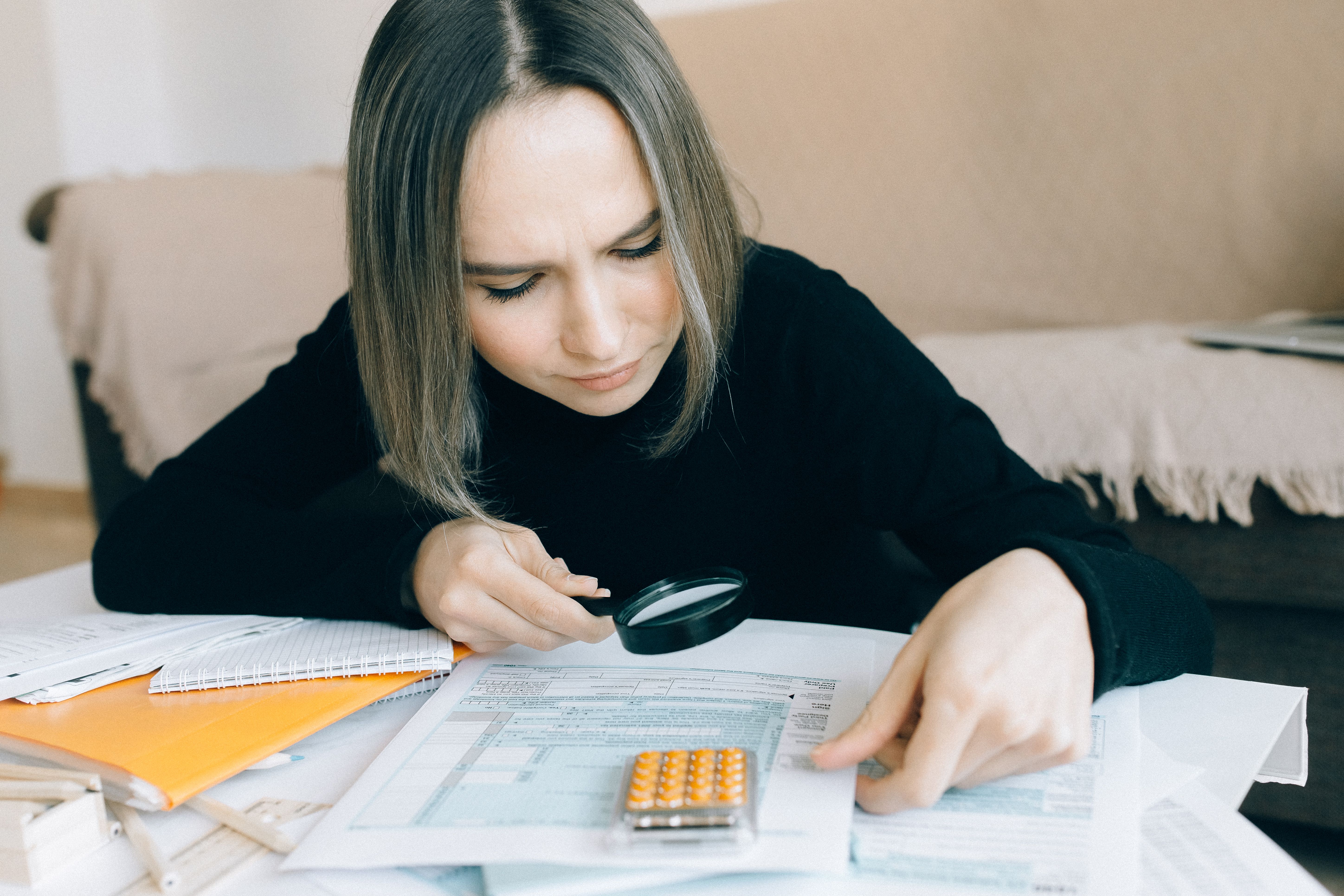 Woman examining documents with a magnifying glass, symbolizing fact-checking and media verification