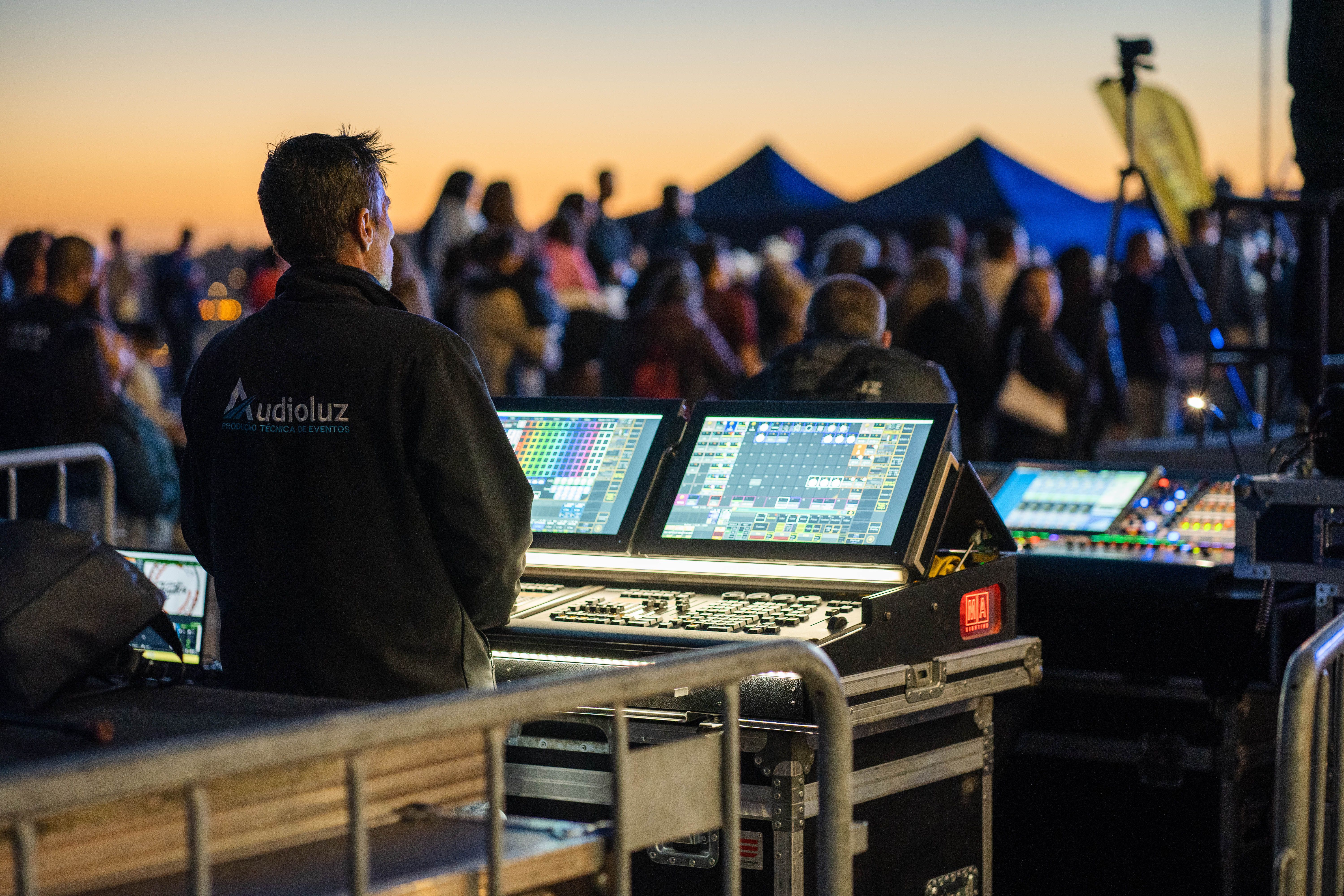 Technician managing sound and lighting equipment during an outdoor event at sunset.